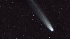 A streak of white across a dark starry night sky shows a comet moving toward the bottom right of the image.