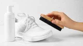 A pair of white mesh shoes next to a hand holding a brush