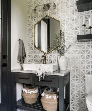 bathroom with black vanity, lattice marble wall tiles on one wall, mirror, sink, lighting, baskets,