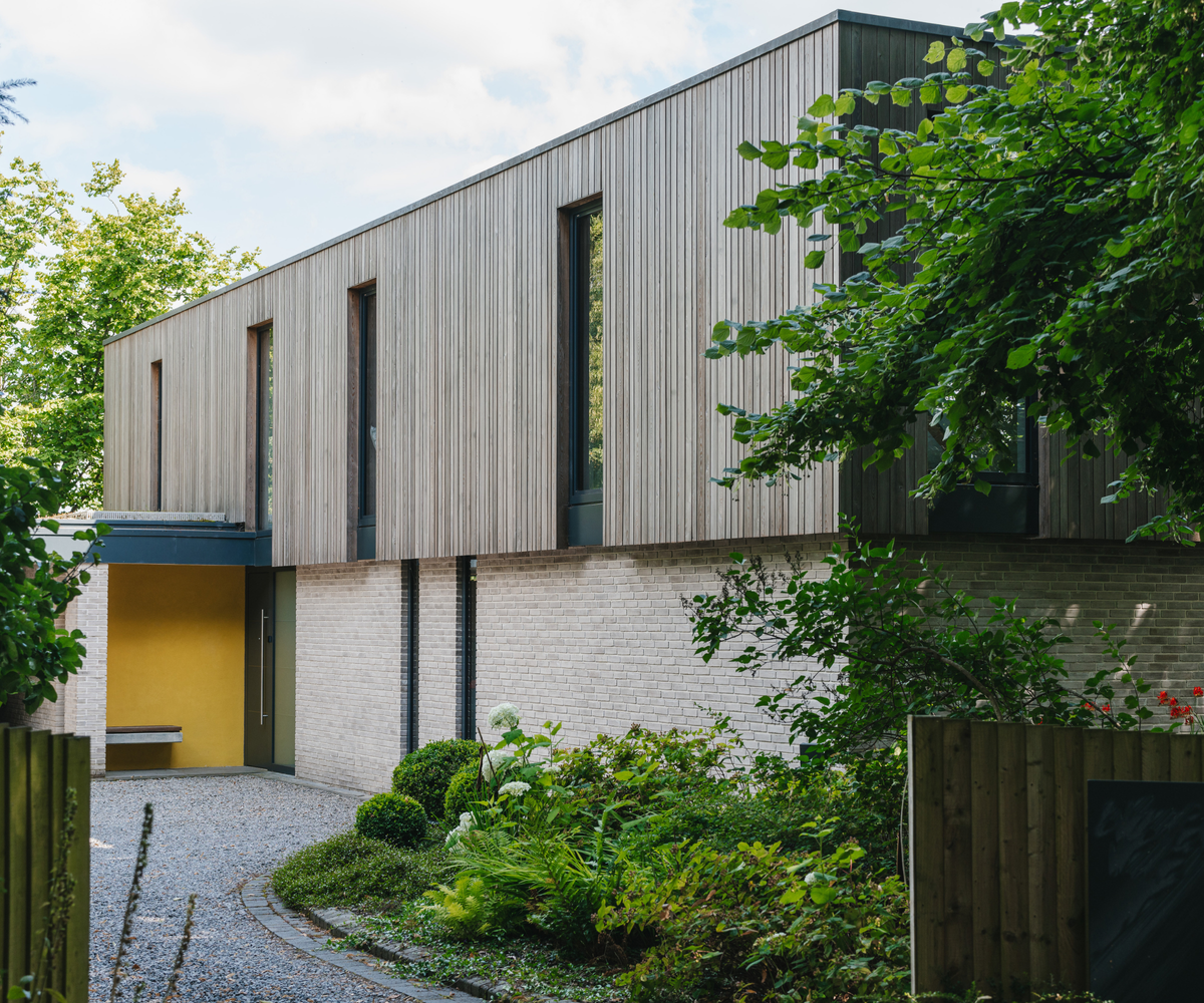 Exterior of a cladded path with a yellow wall and seating area next to the door and a gravel pathway leading up to it