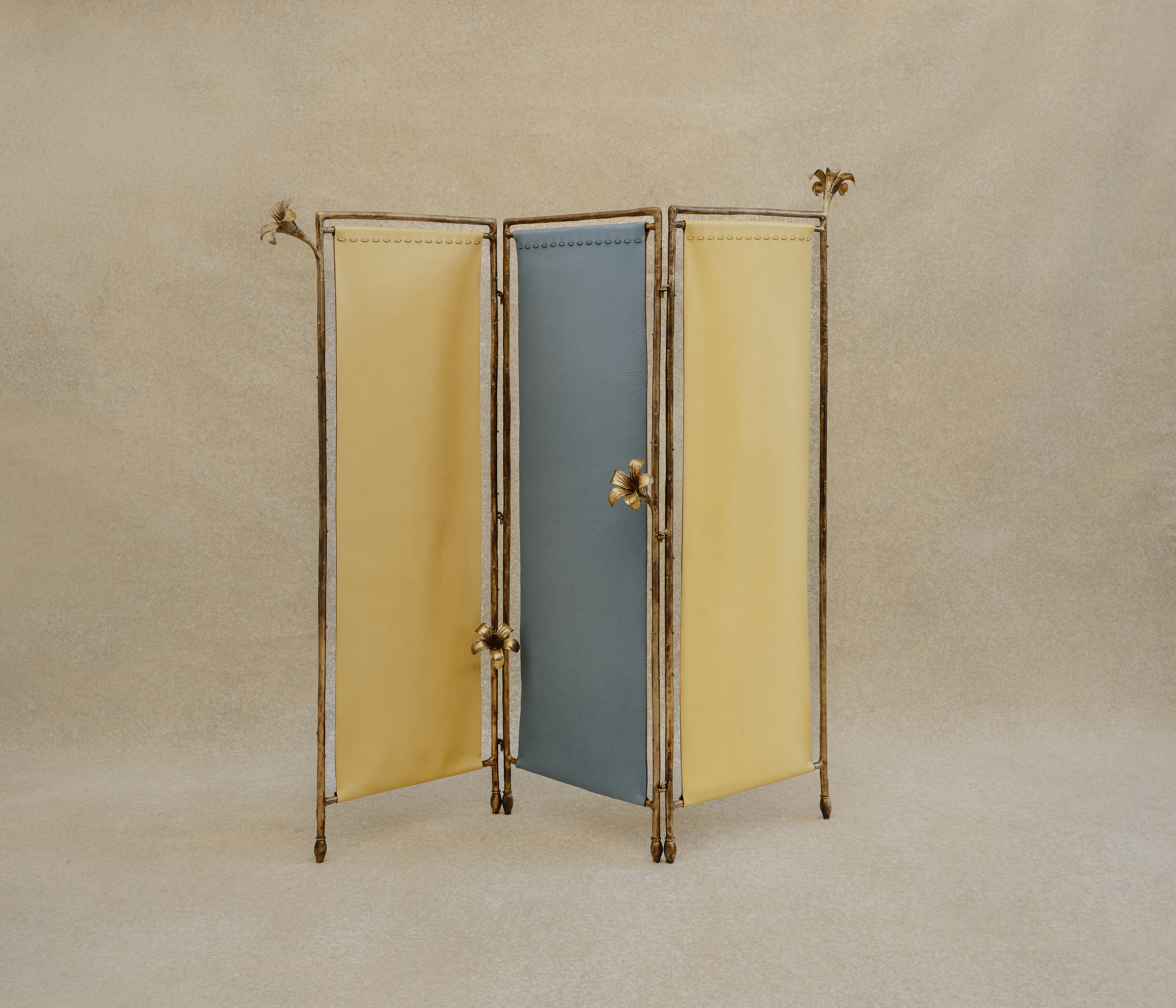 A bronze and textile separee features yellow and teal panels in a pastel palette and flowers-decorated fragments against a beige background.