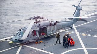a helicopter on a ship deck, at sea. an astronaut in a chair is surrounded by people