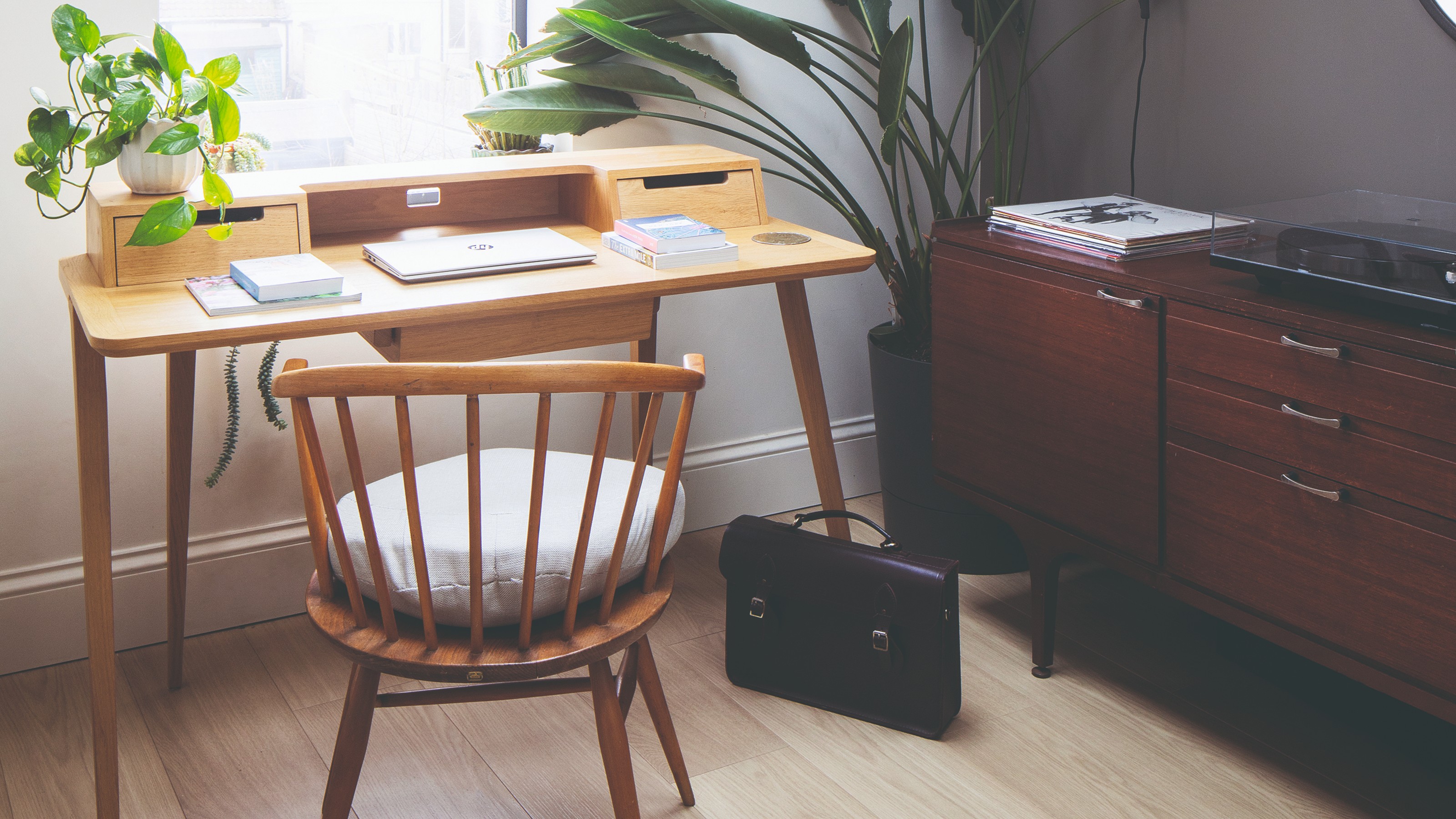 A home office with a Scandi-style storage desk, a wooden desk chair and midcentury sideboard used for storage