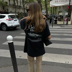 Woman walks down a street in Paris in a vintage black t-shirt, patterned pants and ballet flats. 