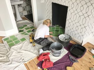 A woman tiling a fireplace with green tiles