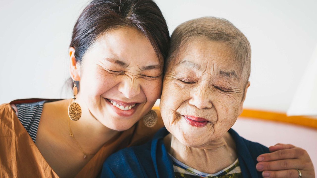 A mom and grown daughter smile and hug.