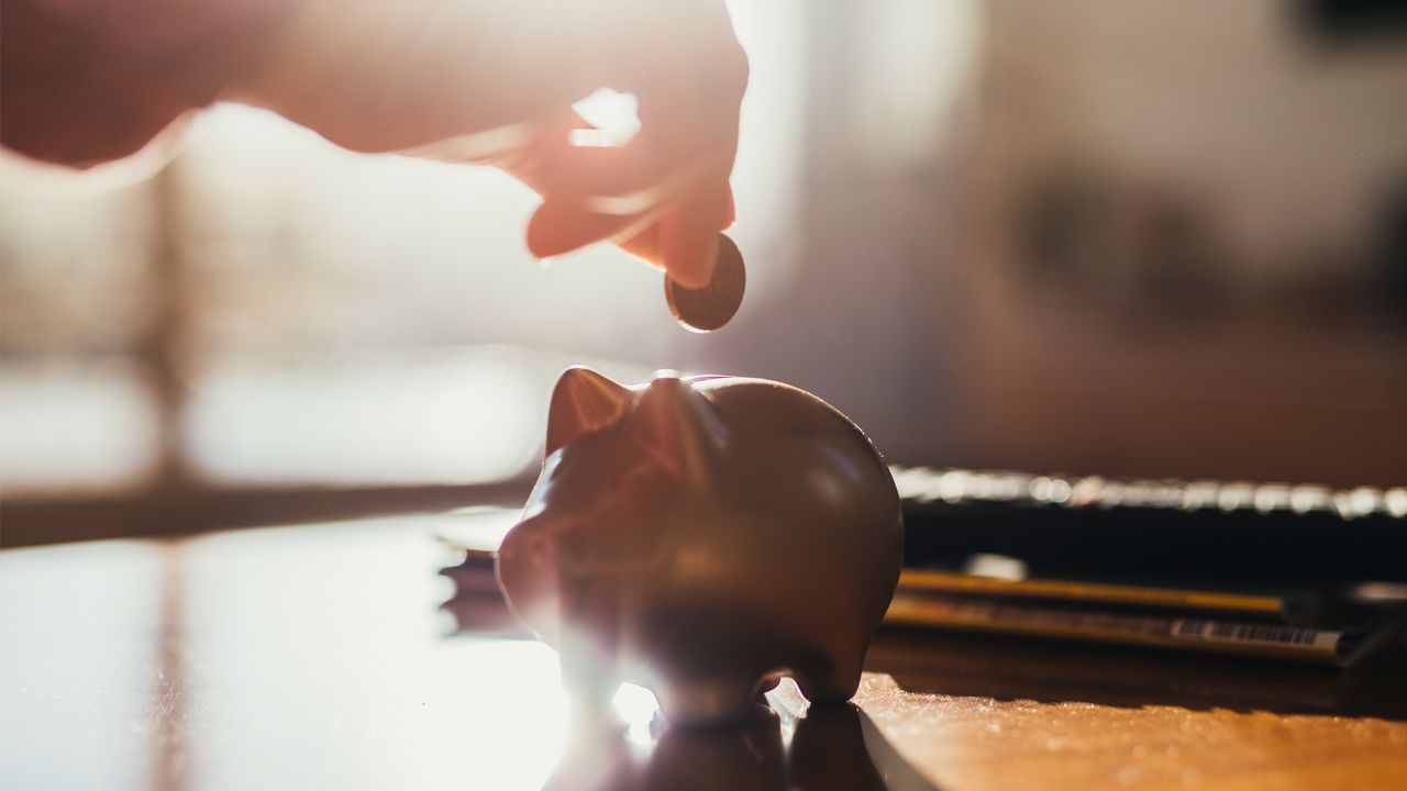 Hand and a piggy bank and coin on a table in backlight