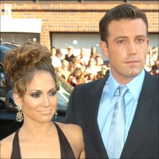 Jennifer Lopez wears a brown dress and wears her hair in an up-do as she poses on the Gigli red carpet with Ben Affleck, who wears a suit with a bright blue shirt and tie