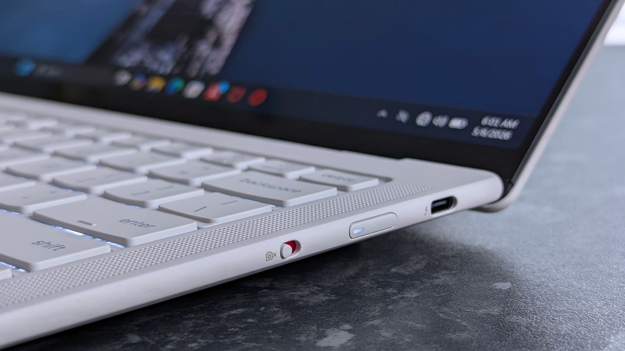 Close-up of a Lenovo Yoga Slim 7i Ultra (Gen 11) Aura Edition laptop with a focus on its side panel, showing a USB-C port and an accented webcam privacy switch. The screen displays app icons.