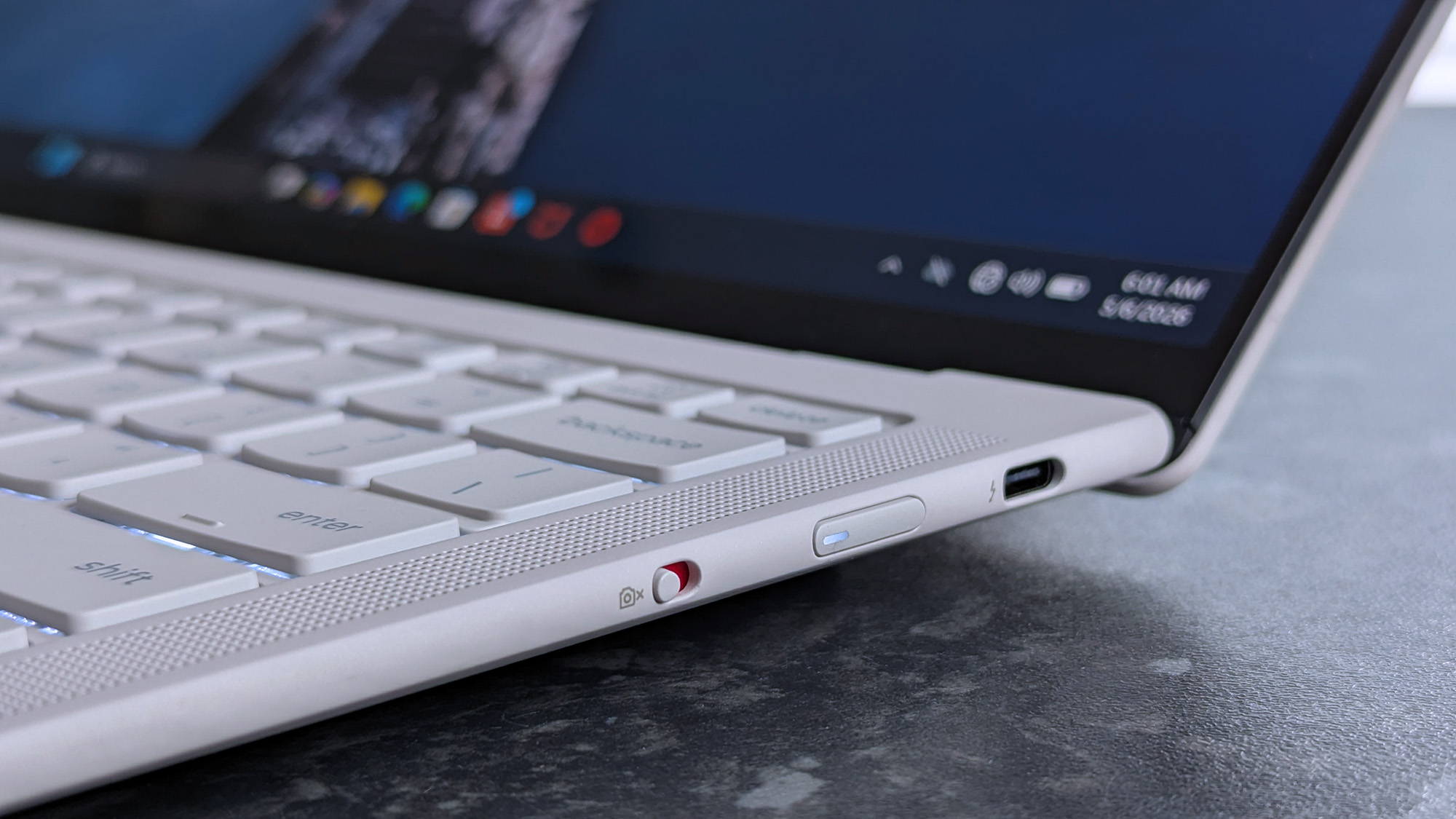 Close-up of a Lenovo Yoga Slim 7i Ultra (Gen 11) Aura Edition laptop with a focus on its side panel, showing a USB-C port and an accented webcam privacy switch. The screen displays app icons.