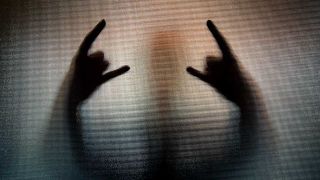 The shadow silhouette of a person performing the heavy metal sign of the horns hand gesture, behind frosted glass. 