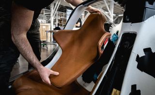 A man fitting a brown leather seat into a car