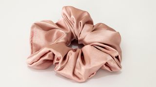 A large pink silk scrunchie is pictured on a white backdrop