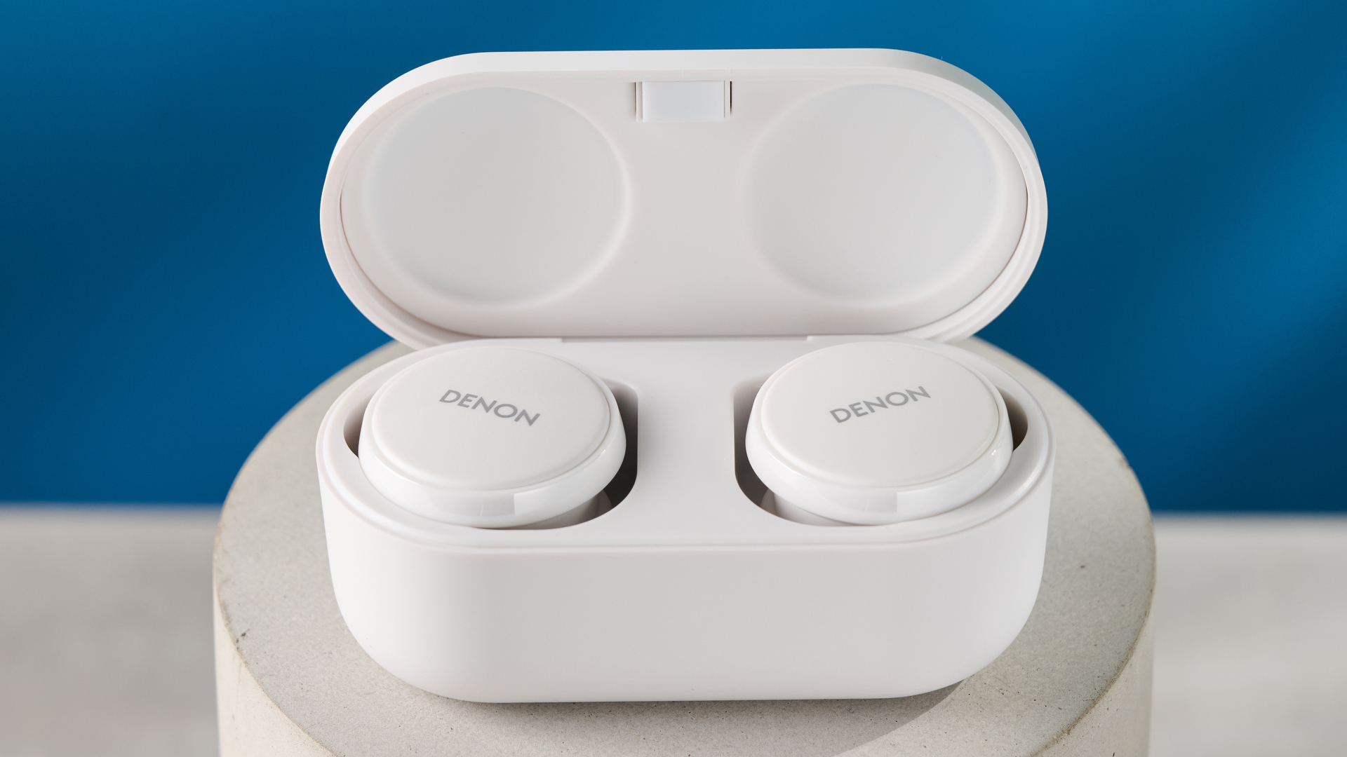 the denon perL Pro wireless earbuds in white, with circular earbud shapes, and a white charging case, photographed against a blue background