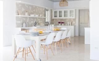 White table and chairs in a kitchen area with neutral tones. Worktop space and shelving with kitchen utensils