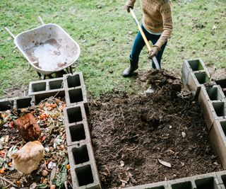 Woman scoops compost from a bin into a wheelbarrow