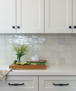 A kitchen counter with tile backsplash and white cabinetry on the top and bottom