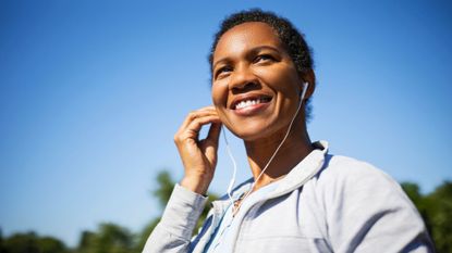 Woman putting headphone into ears in sunshine