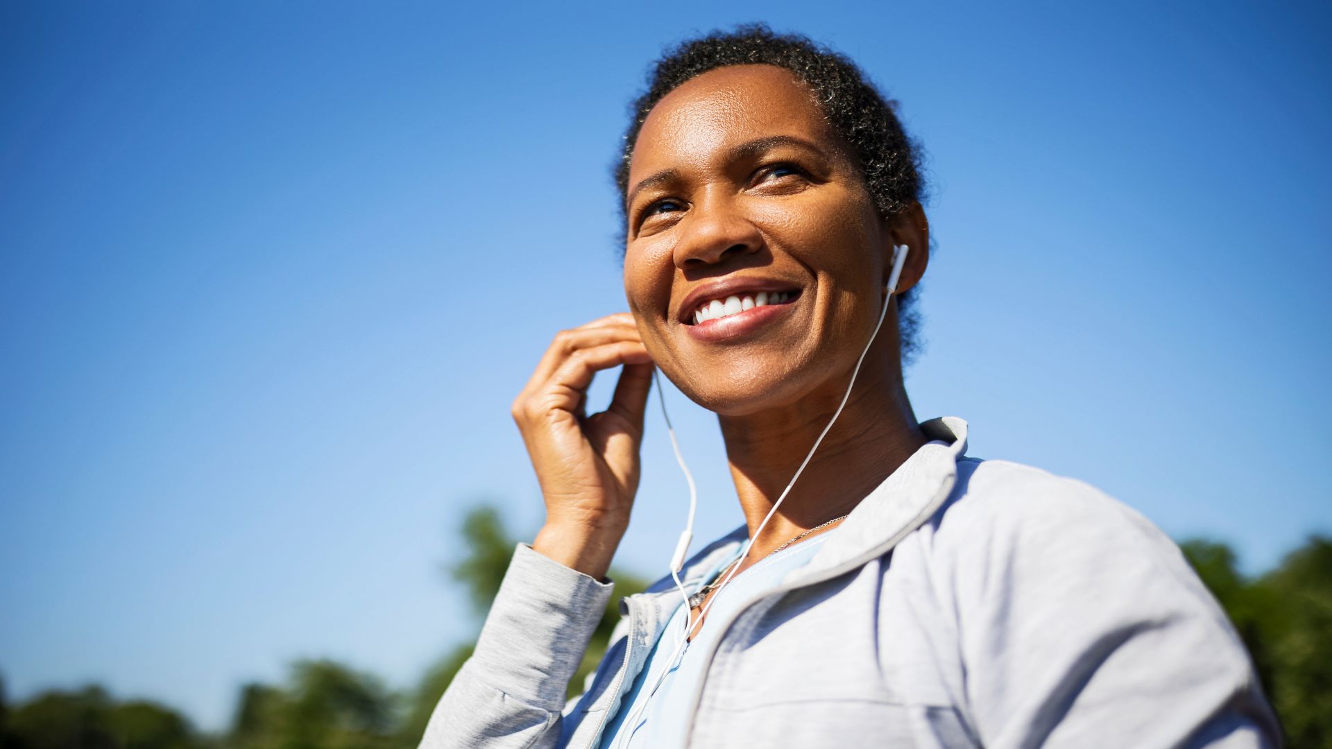 Woman putting headphone into ears in sunshine