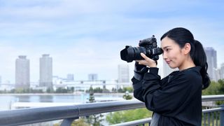 A female photographer uses a Nikon camera in front of a Japanese skyline