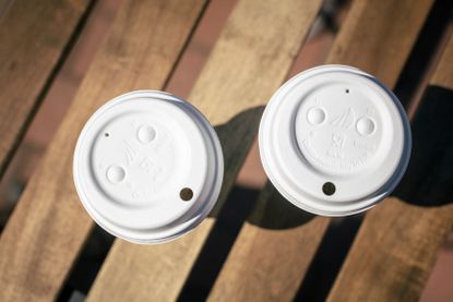 Close up image of two white lidded cups on a wooden slat surface, red floor below