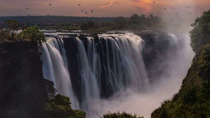 Victoria Falls in Zambia at sunset with birds flying around it