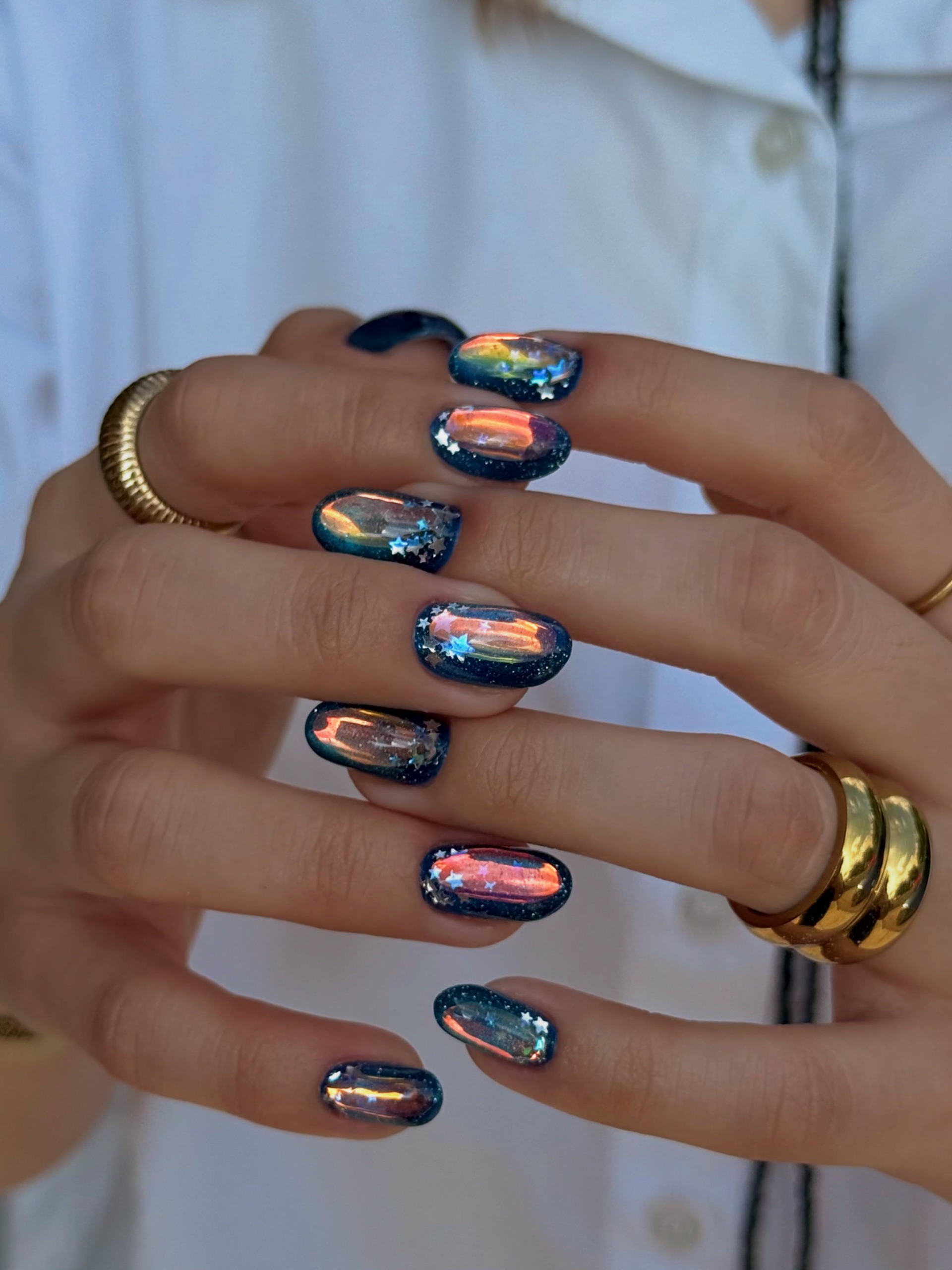 super shiny iridescent chrome nails reflecting pink orange and blue with darker edges and stars