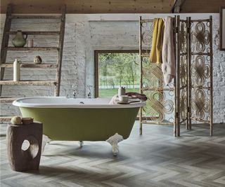 green freestanding bath in room with white painted brick wall and herringbone floor