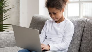 Young girl using a laptop on a gray sofa
