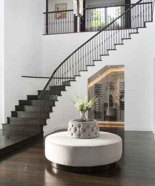Modern entryway bench ideas with a curved staircase, white walls, wine cellar under the stairs and a circular grey upholstered bench