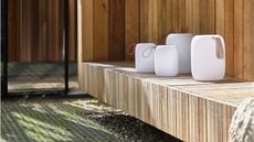 Image of four white lantern lights in different sizes on a wooden bench outside a wooden house.