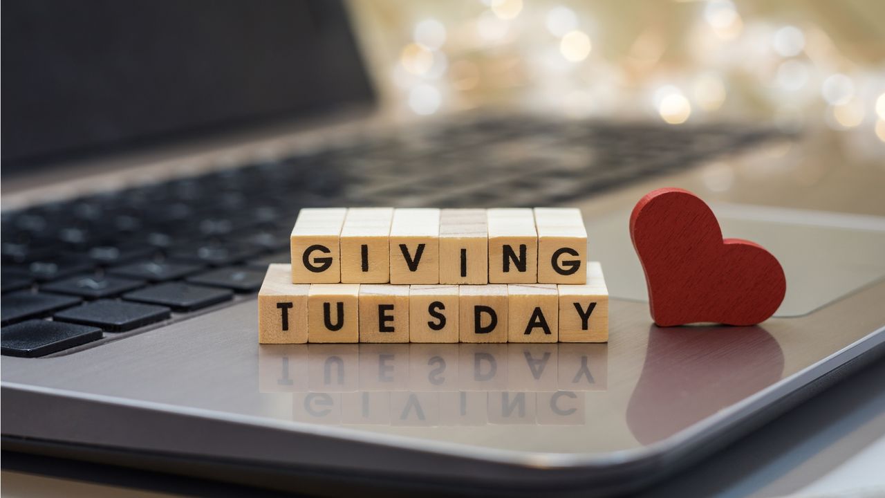 Blocks sitting on the keyboard of a laptop spell out Giving Tuesday next to a red wooden heart.