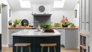 white kitchen with sloping ceiling and rooflights and narrow kitchen island with green and wooden stools