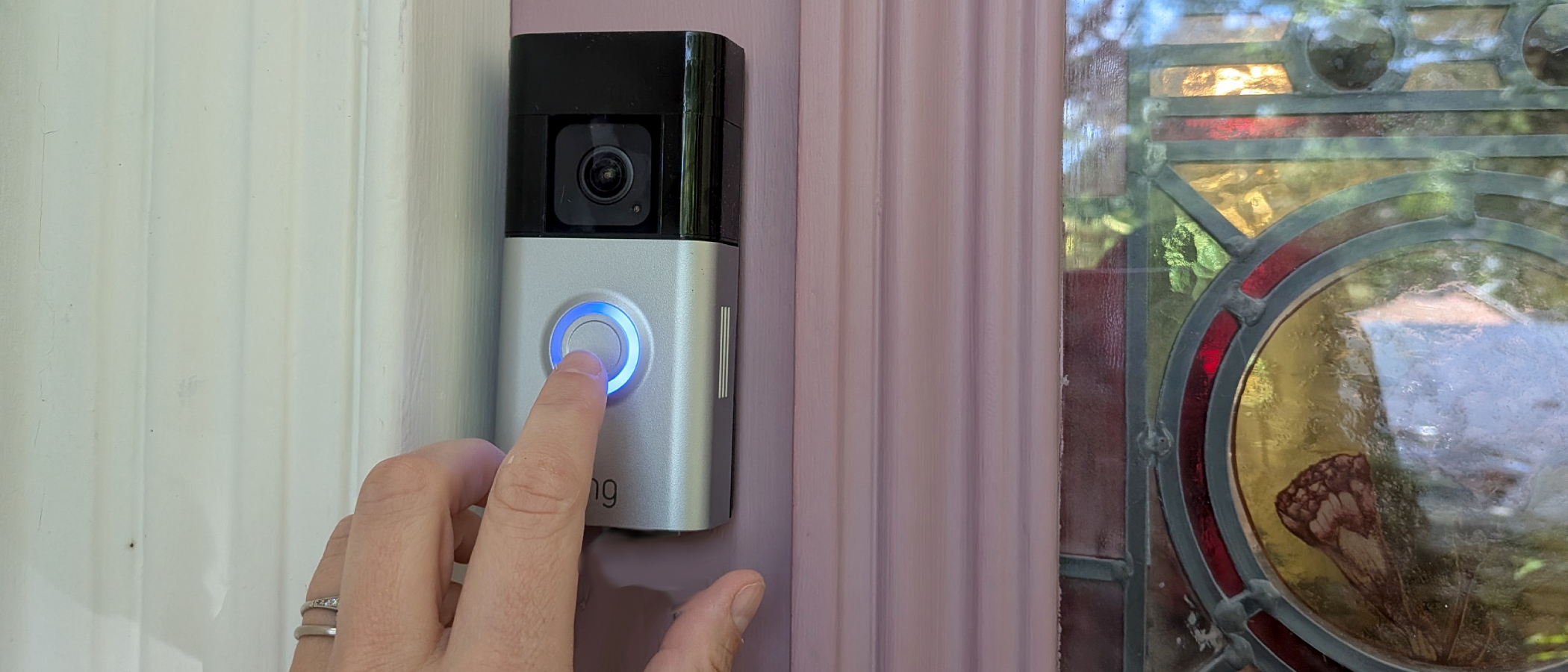 hand pressing ring doorbell on pink front door frame with stained glass insert