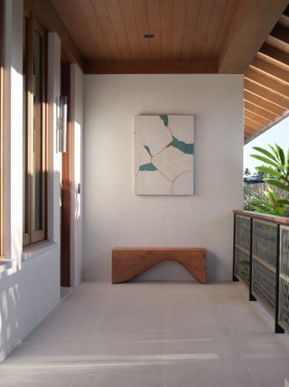 A connected balcony space with a wooden bench. Artwork also hangs on the wall above the bench.