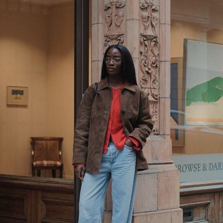 London woman wears light wash baggy jeans with a red cardigan, brown suede jacket and loafers.