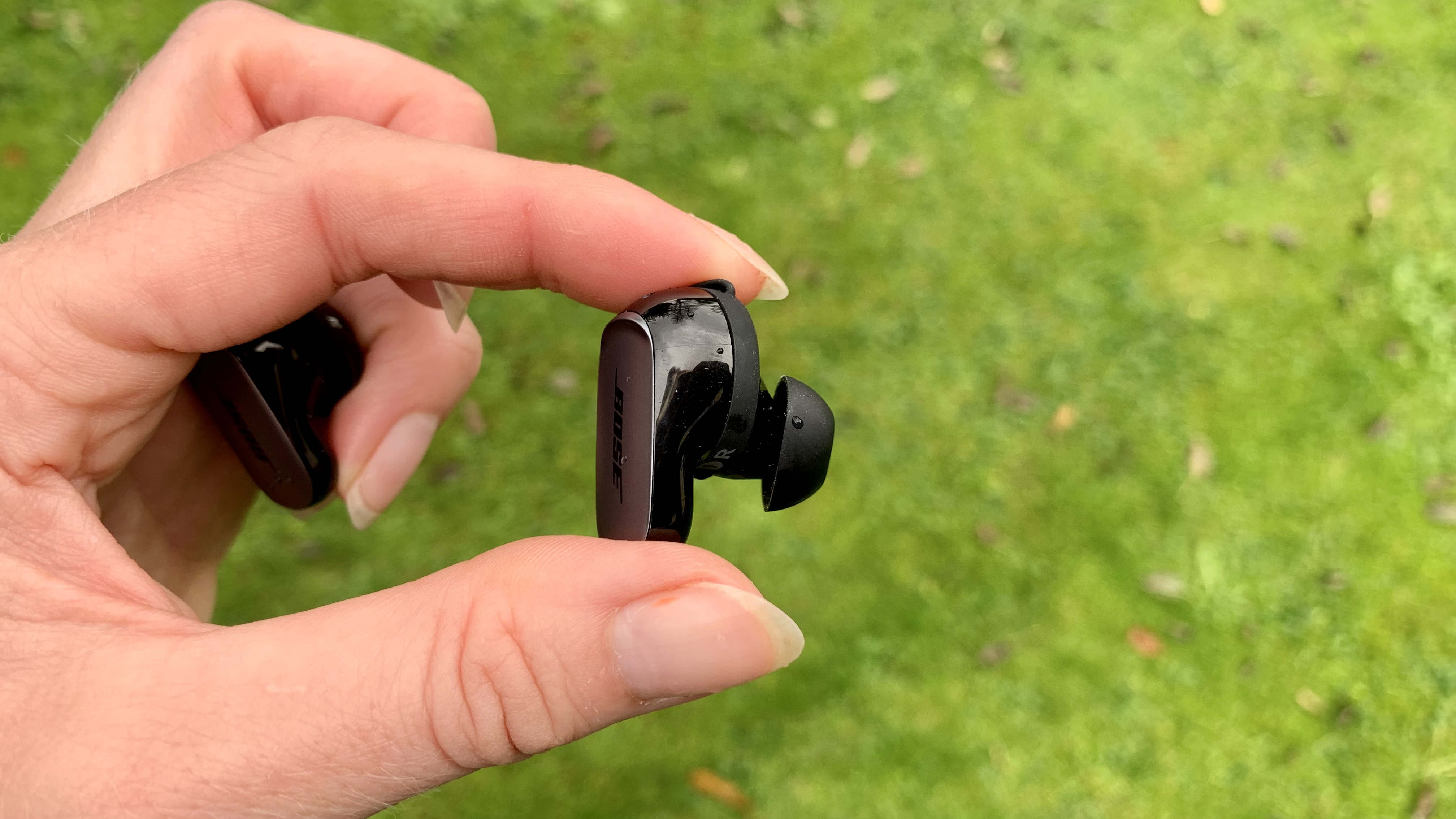 Bose QuietComfort Ultra Earbud held in a hand, on grassy background