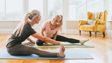 Two women sat on yoga mats stretching out their hips