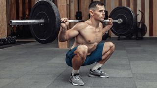 Man at the bottom of a barbell back squat during gym workout