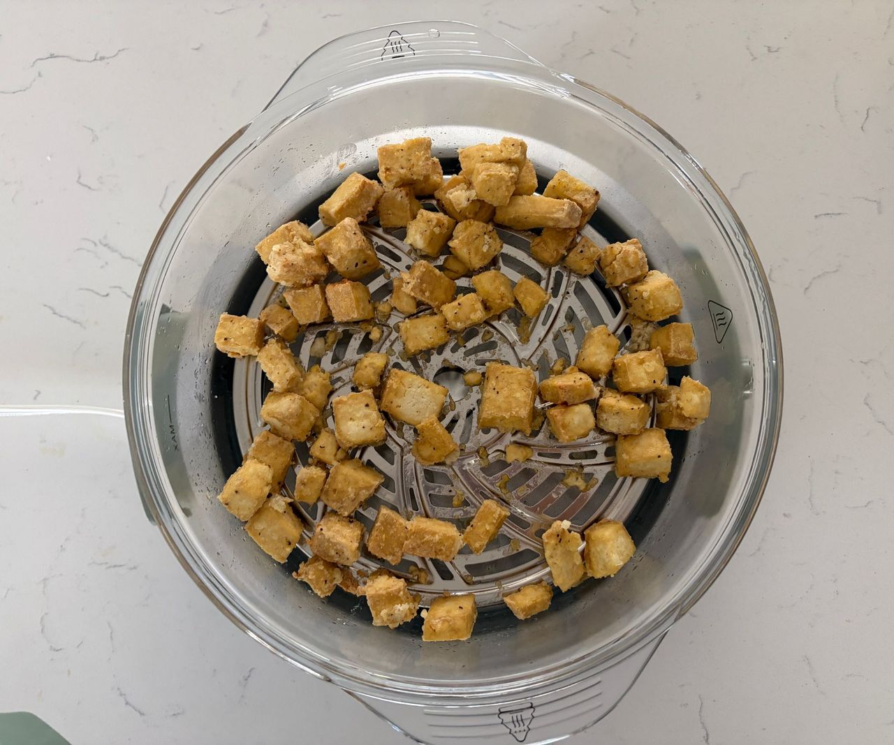 Golden tofu in a glass air fryer basket viewed from above.