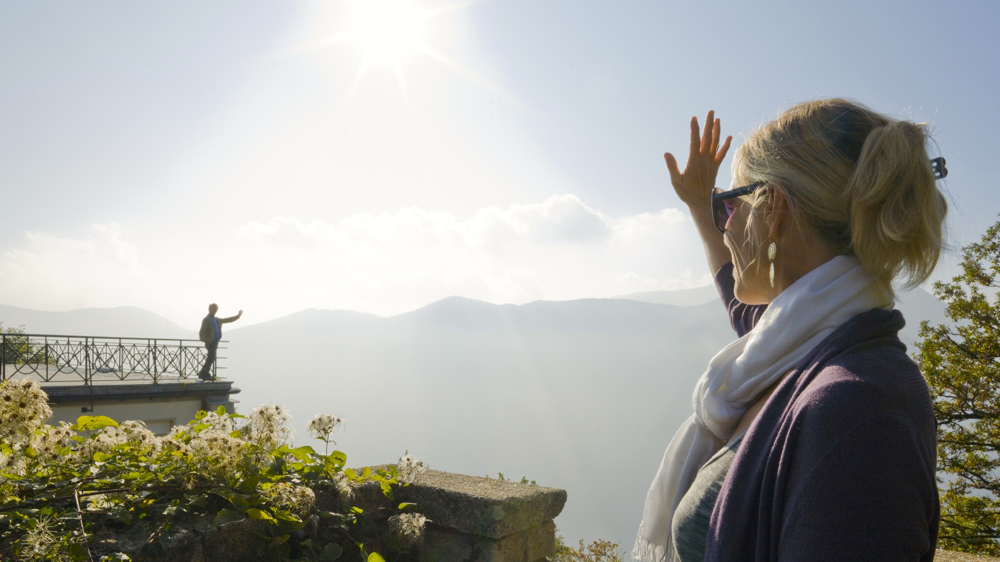 A man waves to a woman from a balcony above Lake Lugano, Italy.