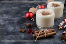 Two glasses of eggnog next to cinnamon sticks and Christmas decorations