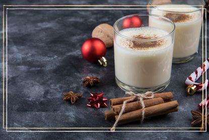 Two glasses of eggnog next to cinnamon sticks and Christmas decorations