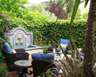 A backyard with tiled fountain, lots of blue and black seating, and a living wall