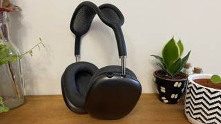 A black pair of Apple AirPods Max headphones on a wooden surface next to some pot plants.