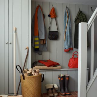 A hallway with a wall covered in grey wood panelling matching a built-in wardrobe and a storage bench with coat hooks on the wall