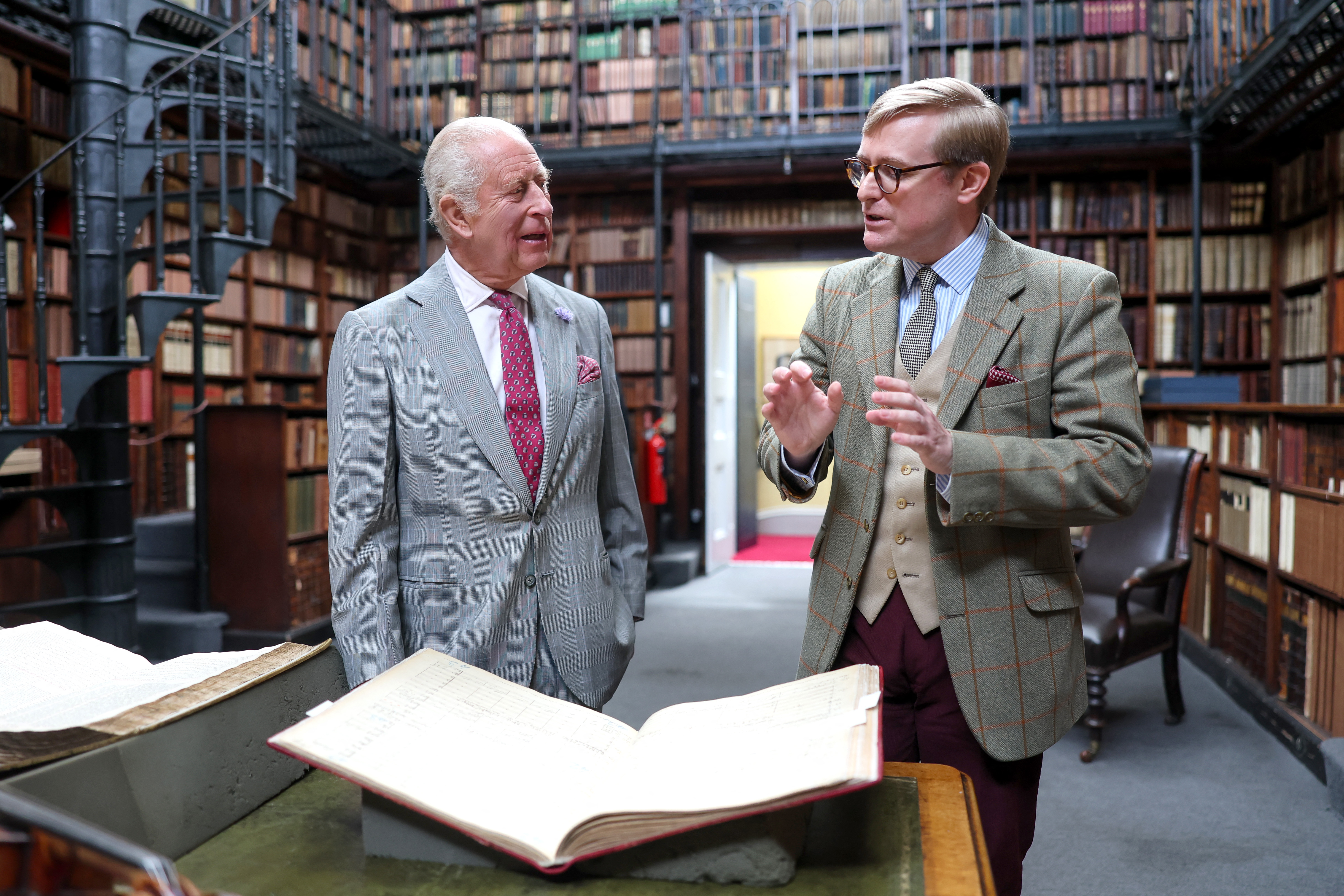 King Charles talking to a man in a library standing in front of an open book