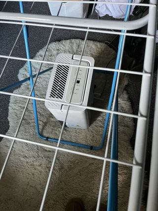 A dehumidifier underneath a clothes drying rack on a white fluffy rug