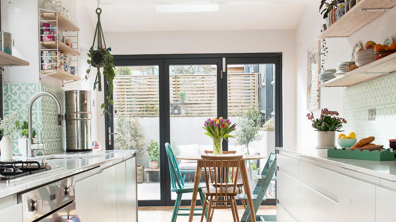 White galley kitchen with open shelving and small wooden dining table