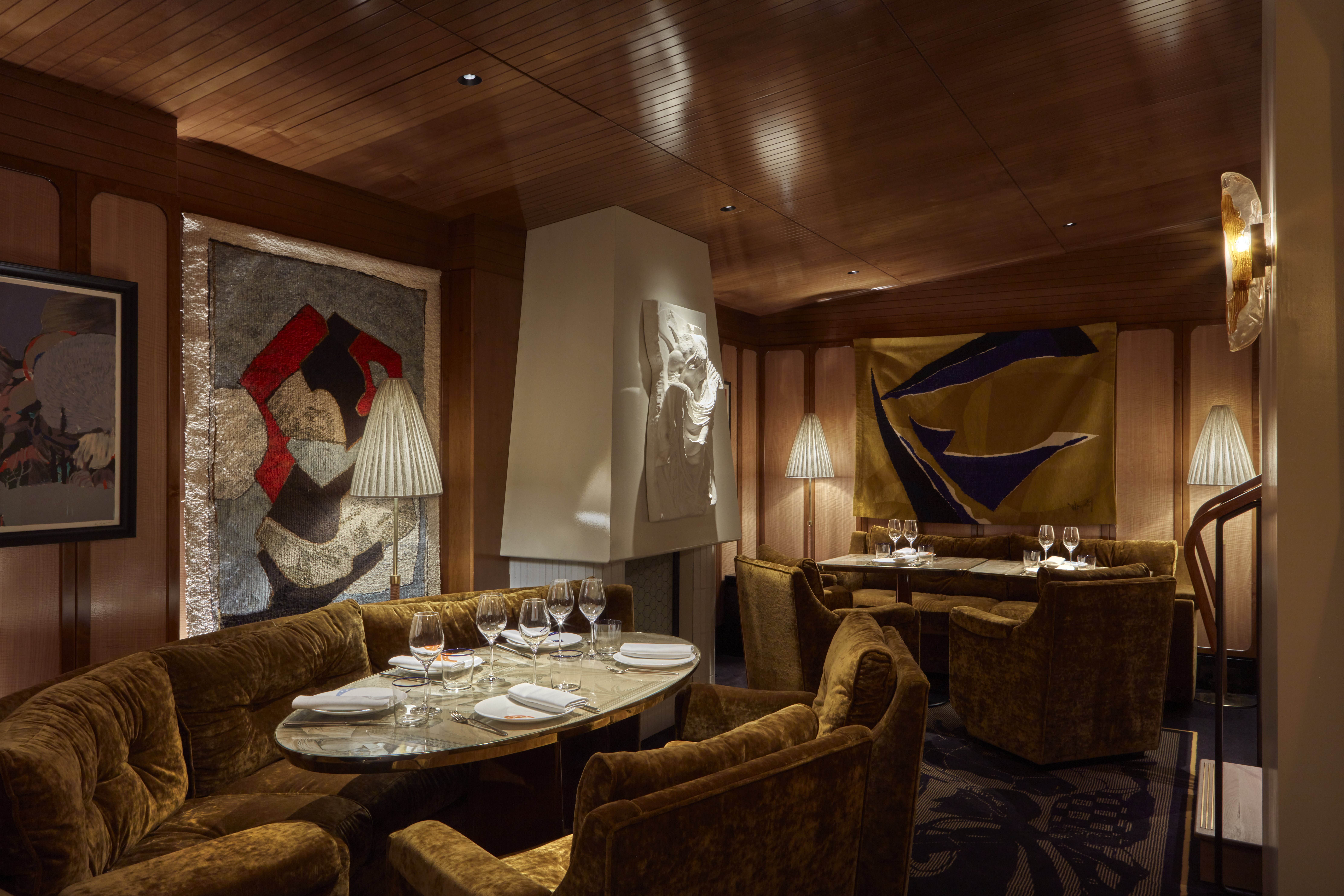 A golden-lit restaurant dining room draped in plush fabrics, velvety banquettes, and colorful artworks, as well as sculptures.